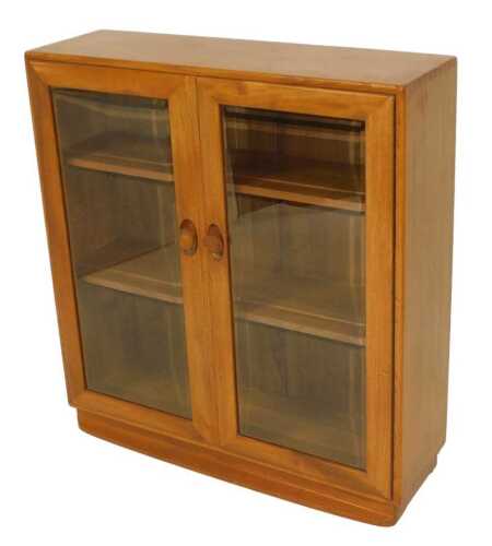 An Ercol light elm bookcase, with two glazed doors enclosing two shelves, raised on a plinth,...