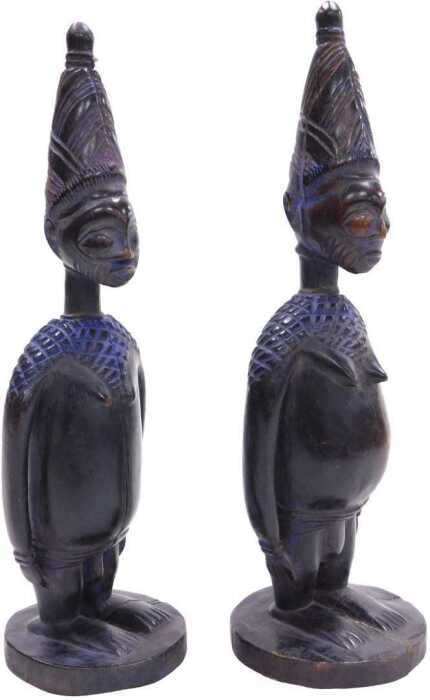 A pair of African Yoruba fertility figures, each with a tapering hat, and circular base,...