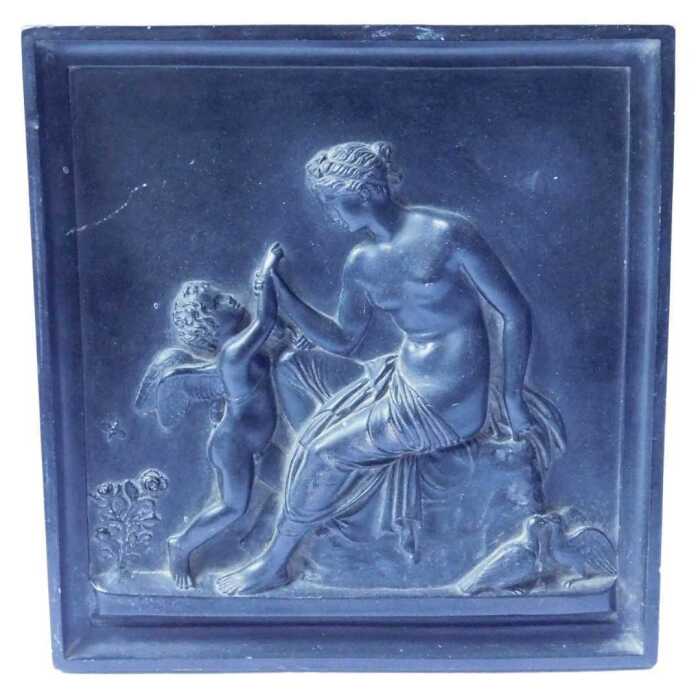 A composition square plaque, decorated in the Neoclassical style with a nude female and a cherub,...
