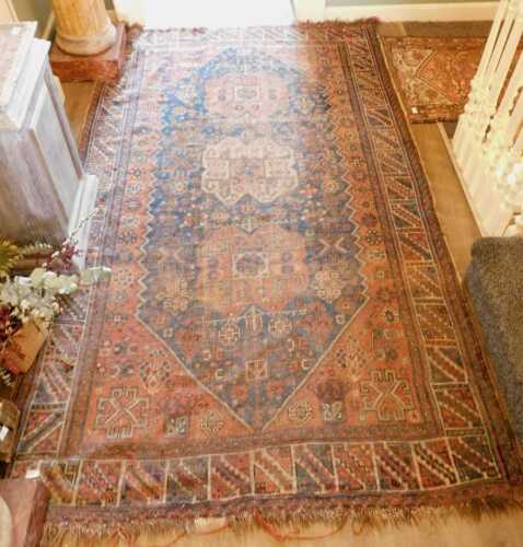 A Persian Caucasian rug, with a design of three medallions, in red and cream, on a navy blue...