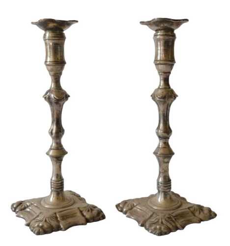 A pair of silvered metal candlesticks, in early Georgian style, the square sconce cast with...