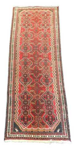 A Persian runner, decorated with geometric devices, on a deep red ground, with three narrow...
