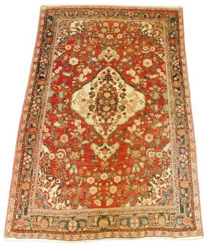 A Persian rug, with a central medallion in cream, on a red ground, with one wide and two narrow...
