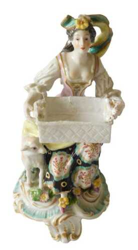An English porcelain figure of a lady holding a basket beside a lamb, on a rococo scroll base,...