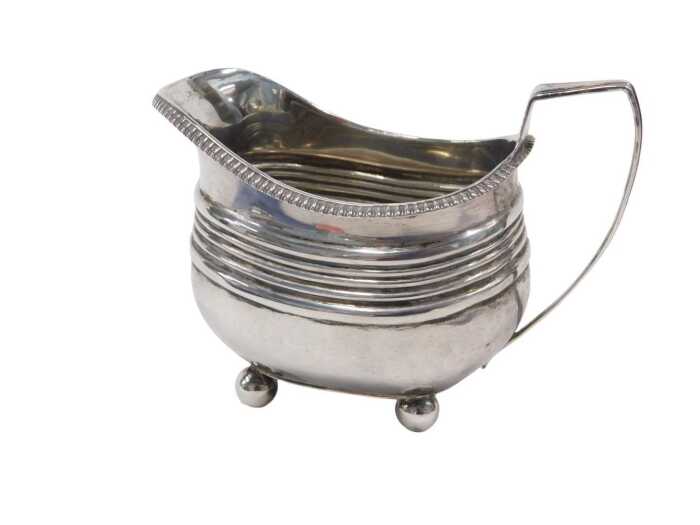 A George III silver milk jug, with strap angular handle, gadrooned rim and reeded body on...