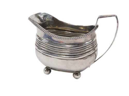 A George III silver milk jug, with strap angular handle, gadrooned rim and reeded body on...