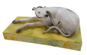 A Derby porcelain figure of a seated greyhound, with hind leg itching ear, in red collar on...