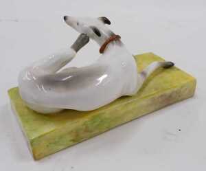 A Derby porcelain figure of a seated greyhound, with hind leg itching ear, in red collar on... - 2
