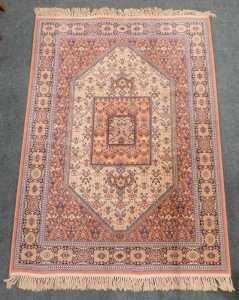 A 20th machine woven rug, the outer field with a geometric floral pattern, in cream, the inner...