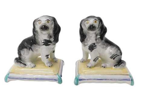 A pair of Staffordshire style spaniel figure groups, each dog seated on cushions, predominantly...