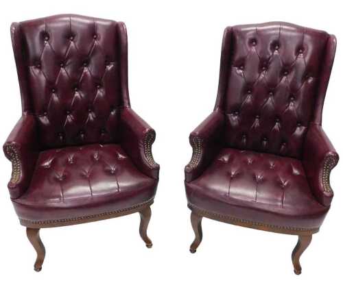 A pair of club style shallow wing armchairs, with button back and seat, overstuffed in crimson...
