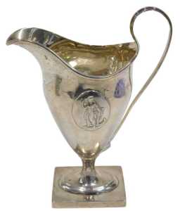 An Edward VII silver cream jug, with strap handle, helmet shaped body, inverted stem and oval...
