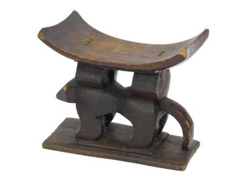 An African Ashanti carved stool, with curved seat, on carved animal support, with rectangular...