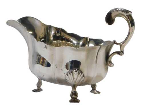 An Edward VII silver sauce boat, of fluted form, with leaf cast handle, raised on three leaf...