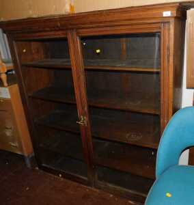 An early 20thC oak bookcase, cornice over two glazed doors with shelf to interior..