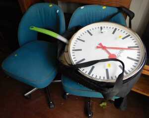 A large Windsor wall clock, two office chairs, and pizza oven pans.