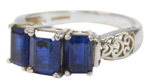 A 9ct white gold three stone dress ring, set with three rectangular cut dark blue stones, in a...