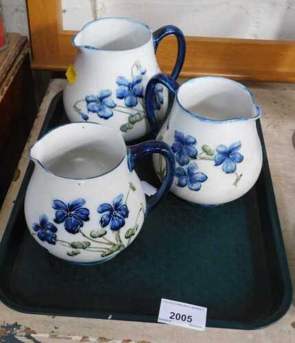 Three James Macintyre and Co Florianware jugs, each decorated with blue violets against a white...