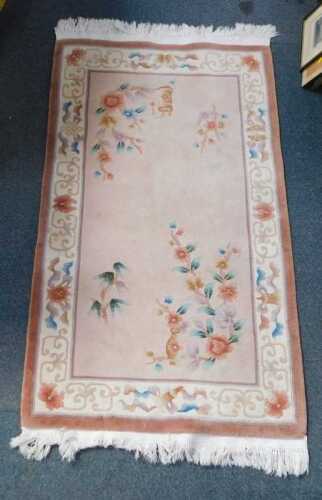 A Chinese wool cut rug, pink ground decorated with flowers.