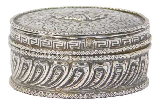 A white metal box and cover, of circular outline, decorated with flower head and scrolls, on a...