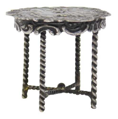 A 19thC silver miniature table, the shaped circular top repousse decorated with figures within...