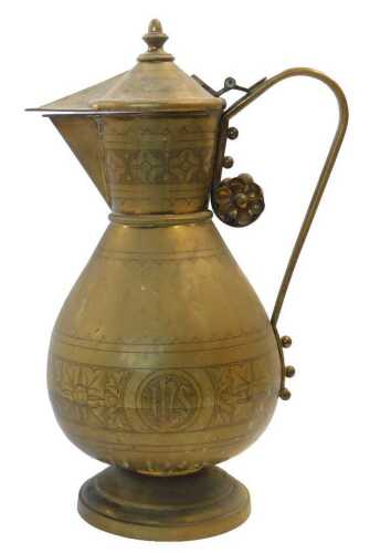 A Middle Eastern brass jug, with a loop handle and pointed spout, body engraved with IHS and the...