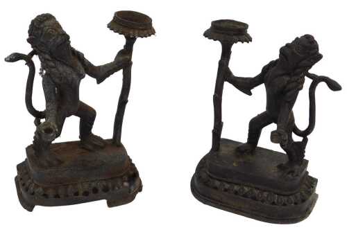 A pair of 19thC Thai bronze candle stands, in the form of standing lions holding flower heads...