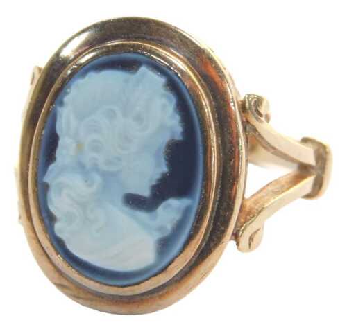 A 9ct gold blue agate carved cameo dress ring, in a raised rub over setting, with heavily scroll...