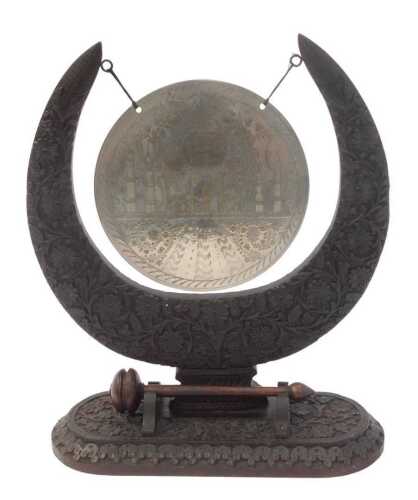 An Indian carved hardwood dinner gong, with a circular metal plate engraved with a depiction of...