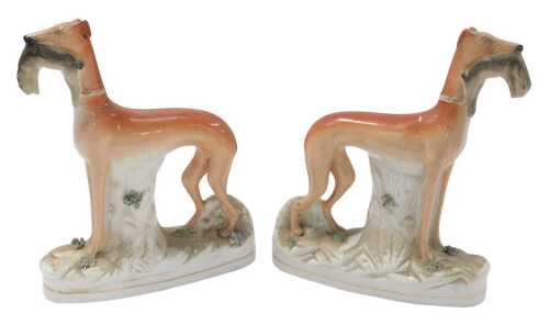 A pair of late 19th/early 20thC Staffordshire flatback greyhounds, each holding a rabbit or hare...