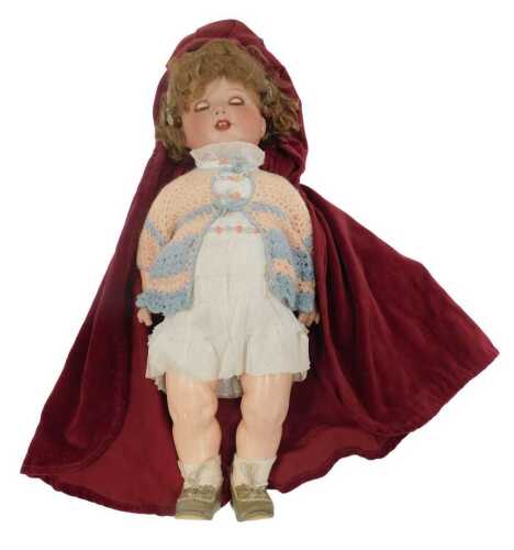 An Armand Marseilles porcelain doll, wearing a red velvet cloak, dress and knitted cardigan,...