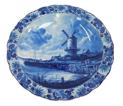 A 20thC Delft pottery charger, decorated centrally with a windmill before a river, within a...