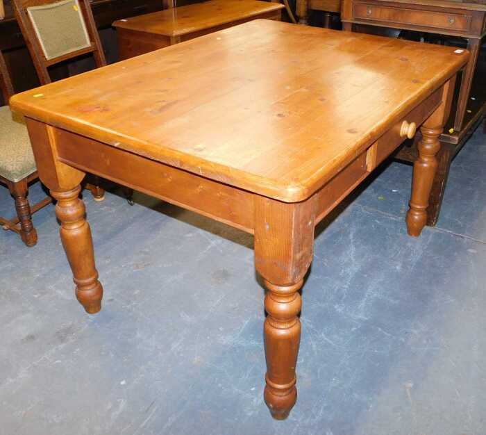 A pine kitchen table, the rectangular top with a rounded edge, above a frieze drawer raised on...