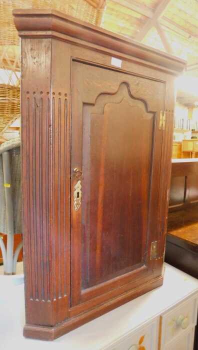 A George III oak hanging corner cabinet, with a moulded top over an arched moulded cabinet door,...