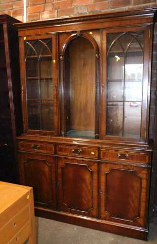 A mahogany display cabinet, the central section with an arched top, and glass shelves, flanked...