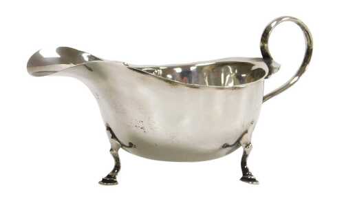 A George V silver sauceboat, with a scroll handle, raised on three hoof feet, Birmingham 1925, 2....
