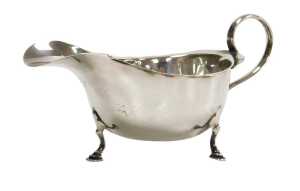 A George V silver sauceboat, with a scroll handle, raised on three hoof feet, Birmingham 1925, 2....