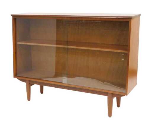 A mid century teak bookcase, with a pair of glass sliding doors, enclosing a single shelf,...