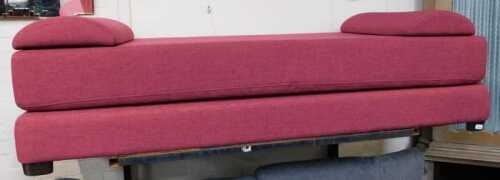 A modern red upholstered daybed, on ebonised feet, 74cm high, 188cm long, 225cm wide.