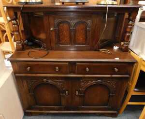 An oak court cupboard, with central door flanked by turned pillars, the base with two drawers...