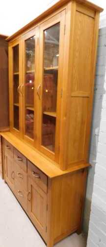 V - A light oak display cabinet, with three glazed doors raised above three central drawers, flanked...