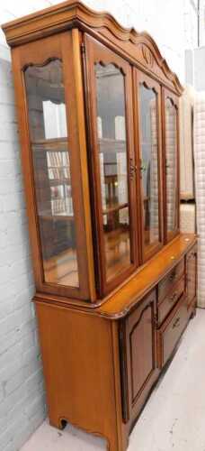 A light wood display cabinet, with three glazed doors, raised above triple drawers flanked by...