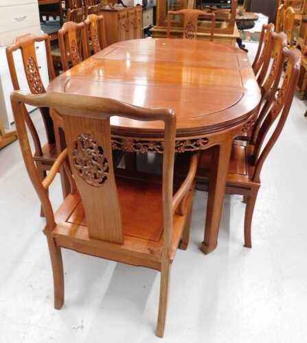 V - An Oriental extending D-end table with heavily carved frieze and eight (6+2) chairs, each with...
