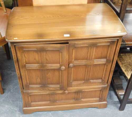 An Ercol television cabinet, with two panelled cupboard doors above a fall, raised on bracket...
