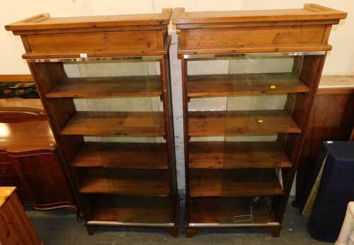 A pair of stained pine bookcases, each with a moulded top above two sliding glass doors, raised...