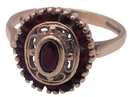 A 9ct gold and garnet ring, the oval cut central garnet in a surround of brilliant cut garnets,...