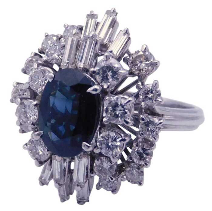 A sapphire and diamond ring, the oval cut sapphire in a tiered claw setting, framed by baguette...