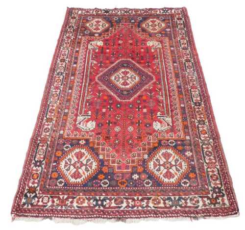 A Persian rug, with a central multicoloured lozenge, on a red ground with further lozenges to...