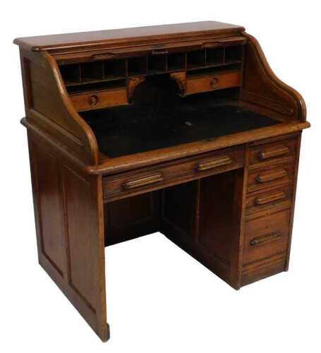 An early 20thC oak roll top desk, the top with a tambour door, enclosing pigeon holes and...