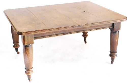 A Victorian oak wind out dining table, with two additional leaves, raised on turned legs, brass...